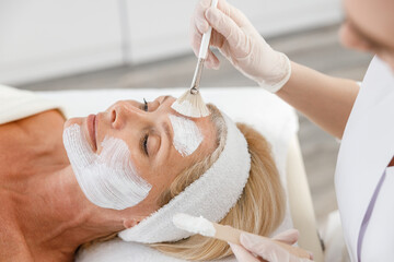 Close up face peeling mask, spa beauty treatment, skincare. Senior woman getting facial care by beautician at spa salon