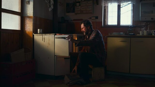 Side view of poor mature man sustaining fire in oven, poverty concept.
