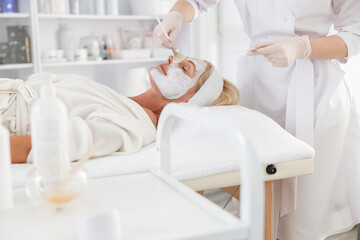 Fototapeta na wymiar Face peeling mask, spa beauty treatment, skincare. Senior woman getting facial care by beautician at spa salon, side view