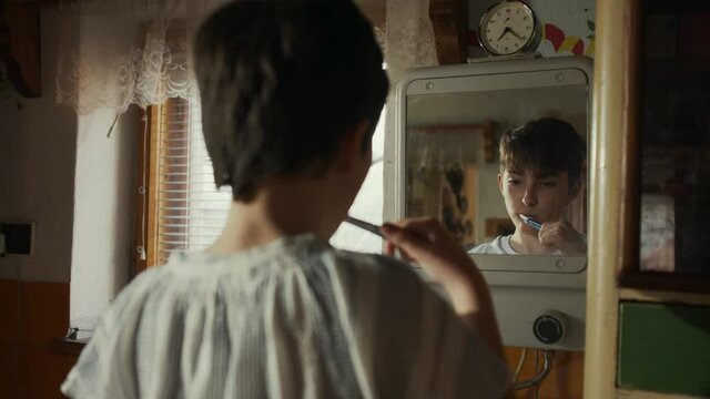 Rear view of poor sad small girl brushing her teeth at home, poverty concept.