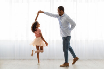 Black father and daughter dancing at home, full length shot