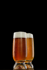 Two glasses of different cold dark beers with strong flavor and high alcohol content in an isolated studio shot over black background.