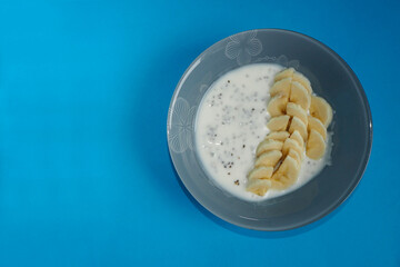 yogurt with sliced banana slices and chia seeds stands in a gray round plate on a blue background top view . natural snack food