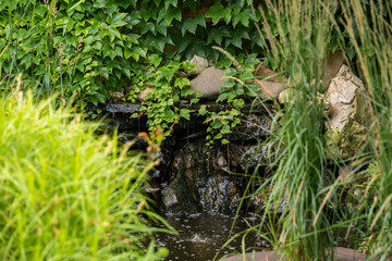 a natural stone pond with fish and a waterfall surrounded by flowers and shrubs in landscape design