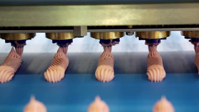 Forming apparatus with a conveyor on which confectionery products are stacked. Sweet pink meringue production line. Shallow depth of field.