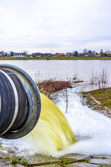 Fototapeta premium Closeup of a water pump pipe with water flowing into the Meuse river, system to control high levels of streams and prevent flooding in Geulle aan de Maas, South Limburg, the Netherlands