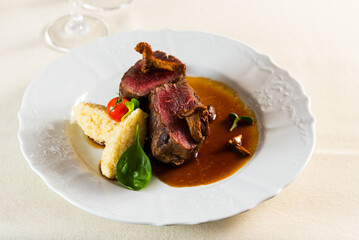 two steaks fried medium in their own juice with a side dish of porridge and garnished with tomato chanterelle mushrooms and basil on a platter in a restaurant