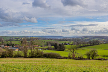 Dutch countryside with hills, green grass, bare trees, farms and small villages in the background, sunny day with a blue sky and white clouds in Valkenburg aan de Geul in South Limburg, Netherlands