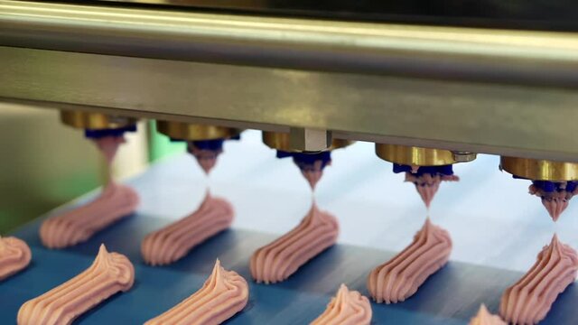 Forming apparatus with a conveyor on which confectionery products are stacked. Sweet pink meringue production line. Shallow depth of field.