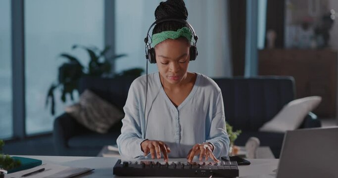 Young african american woman playing on electronic piano synthesizer keyboard enjoying sound recording audiotracks at home. Female musician.