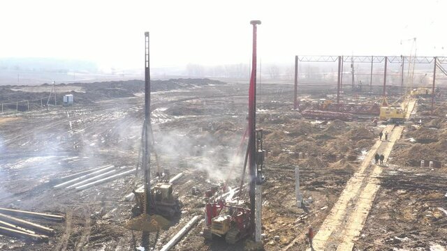Excavation at a construction site, diesel pile driving machine with rumble and smoke drives piles deep into the ground to ensure the strength of the foundation of the future structure