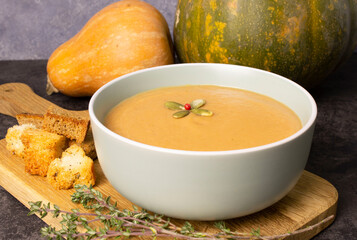 Vegetarian pumpkin cream soup in a bowl on a wooden board with thyme sprigs and breadcrumbs. Soup...