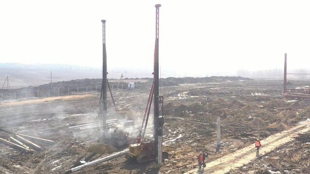 Excavation at a construction site, diesel pile driving machine with rumble and smoke drives piles deep into the ground to ensure the strength of the foundation of the future structure
