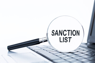 SANCTION LIST text on a magnifying glass that lies on the keyboard of a laptop