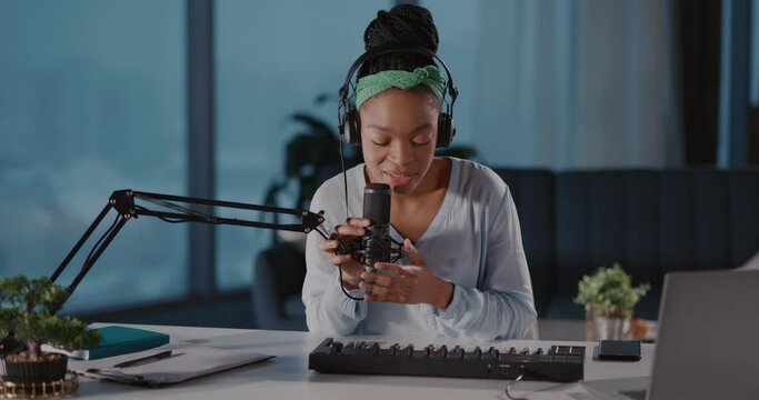 African attractive inspired woman music artist recording audiotrack, singing song and using electronic piano synthesizer keyboard in living room.