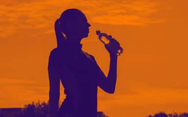 Silhouette of a sportive woman drinks water in training.