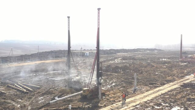 Excavation at a construction site, diesel pile driving machine with rumble and smoke drives piles deep into the ground to ensure the strength of the foundation of the future structure