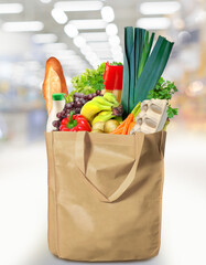 Eco friendly reusable shopping bag filled with bread, fruits and vegetables on a supermarket background