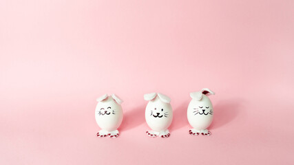 Three cute bunnies made of white chicken eggs isolated on a light pink pastel background. Happy Easter Day.