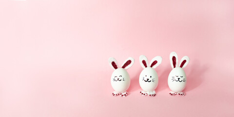 Three cute bunnies made of white chicken eggs isolated on a light pink pastel background. Happy Easter Day.