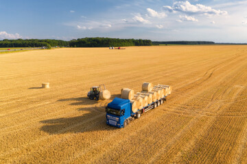 Aerial view of truck with hay bales. Agricultural machinery. Chamfered field and hay stacks after...