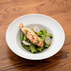 Red fish with green noodles, radishes and microgreens. Healthy food rich in Omega 3 and vitamins. Lunch with seafood and italian pasta. White plate with diet meal on wooden table, top view. 1x1.