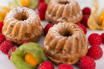 Lovely sweet cakes on white plate with sugar on top, raspberries and golden berries below. Homemade baked sweets for snack or breakfast.
