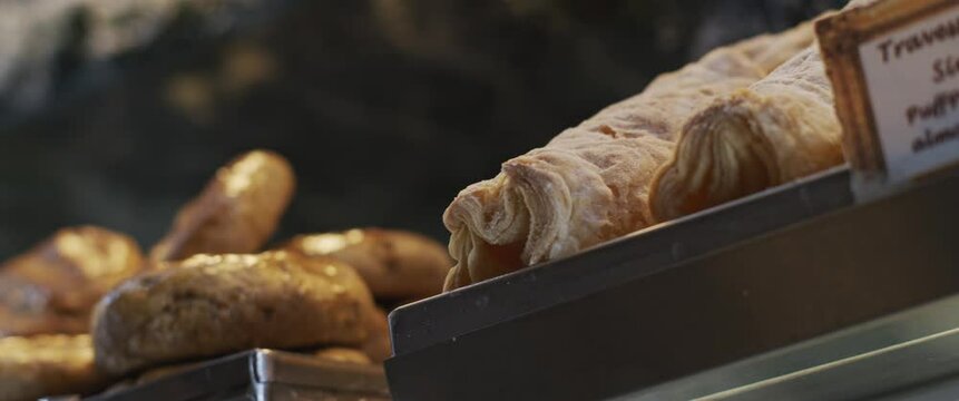 Freshly baked bread and puff pastry desserts in a cafe shop display. Slow motion, close up,