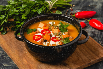 homemade creamy pumpkin soup with toppings on steal bowl with scattered ingredients on kitchen cutting board
