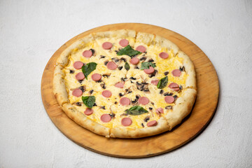 Cut round pizza on wooden board. Delicious hot pizza with melted cheese, mushrooms and sausages on white background. Traditional italian food. Junk food. Horizontal format.