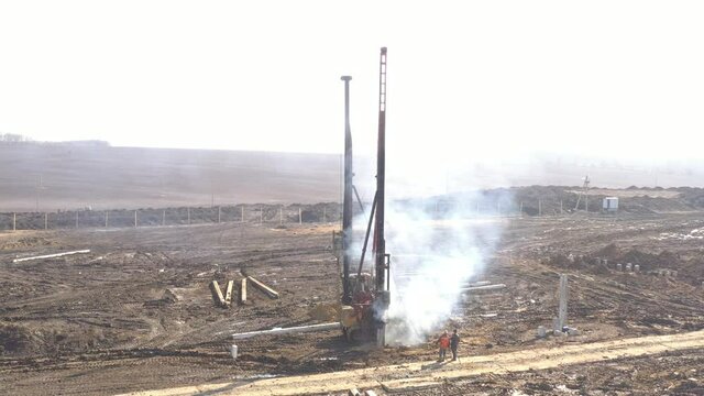Excavation at a construction site, diesel pile driving machine with rumble and smoke drives piles deep into the ground to ensure the strength of the foundation of the future structure