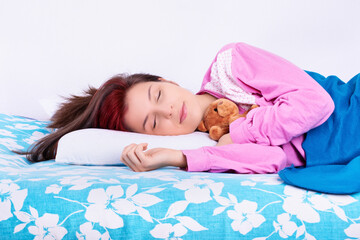 Obraz na płótnie Canvas Young woman sleeping calmly in her bed hugging teddy bear