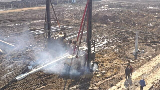 Excavation at a construction site, diesel pile driving machine with rumble and smoke drives piles deep into the ground to ensure the strength of the foundation of the future structure