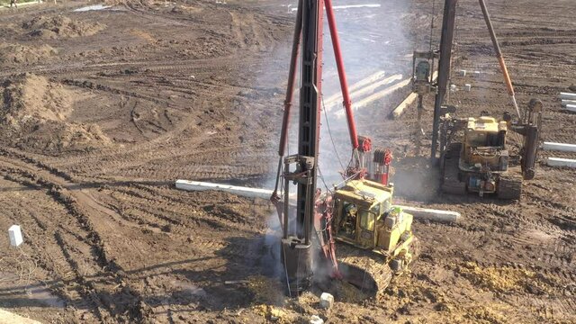 Excavation at a construction site, diesel pile driving machine with rumble and smoke drives piles deep into the ground to ensure the strength of the foundation of the future structure