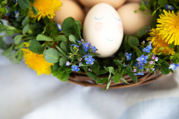 Beautiful spring bouquet in a wooden basket with Easter painted eggs, eggs with cute faces. Easter postcard. Close-up.