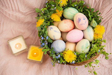 On a pastel bedspread is a basket of grass and bright flowers. The basket contains Easter eggs painted with watercolors in beautiful pastel colors.