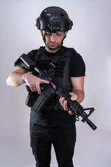 Military male wearing black equipment is looking at his weapon.