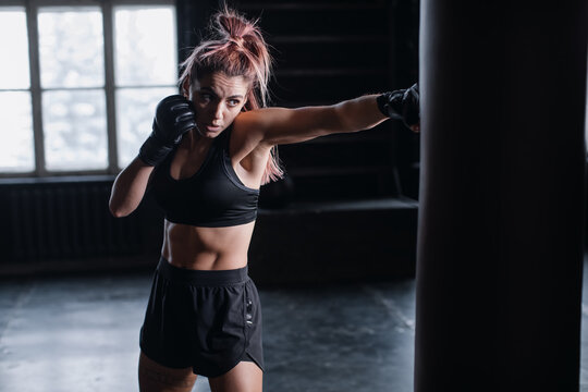 Athletic fit female boxer exercising punches with boxing bag in gym during kickboxing and self defense intensive workout