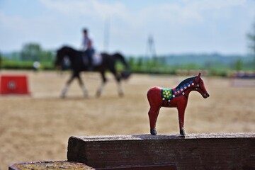 Drewniana czerwona figurka konia. W tle jeździec na koniu.