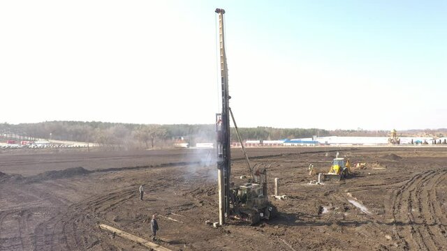 Excavation at a construction site, diesel pile driving machine with rumble and smoke drives piles deep into the ground to ensure the strength of the foundation of the future structure