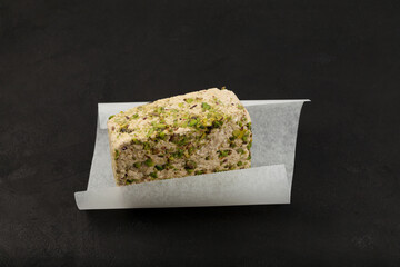Sesame halva with pistachios on white paper, close-up.  Dark textured background, copy space. Middle eastern delicious plant-based sweets