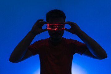 Silueta de un chico con gafas futuristas de luz led en fondo azul.