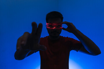 Silueta de un chico con gafas futuristas de luz led en fondo azul.