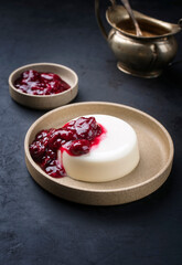 Modern style traditional blancmange almond pudding with sour cherry coulis served as close-up in a Nordic design plate on black background