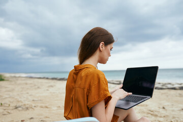 woman tourist sitting on the beach with laptop working