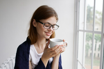 woman with glasses at home near the window with a cup of coffee rest