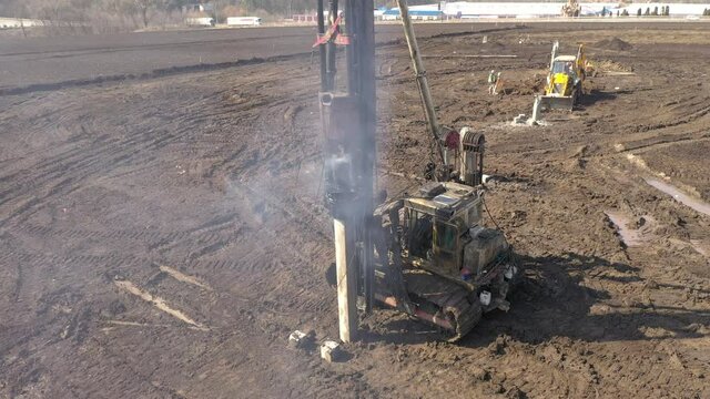 Excavation at a construction site, diesel pile driving machine with rumble and smoke drives piles deep into the ground to ensure the strength of the foundation of the future structure