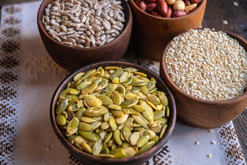 Peeled pumpkin, sunflower, nut, and sesame seeds in a wooden bowl on a wooden table. Bakery ingredients. Products for tasty and healthy food.
