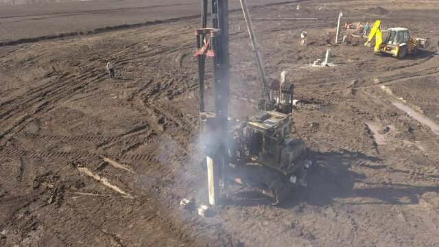 Excavation at a construction site, diesel pile driving machine with rumble and smoke drives piles deep into the ground to ensure the strength of the foundation of the future structure