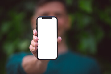 Man holding modern smartphone with mockup screen or blank screen. Young man showing his phone with blank space outdoors on a green background